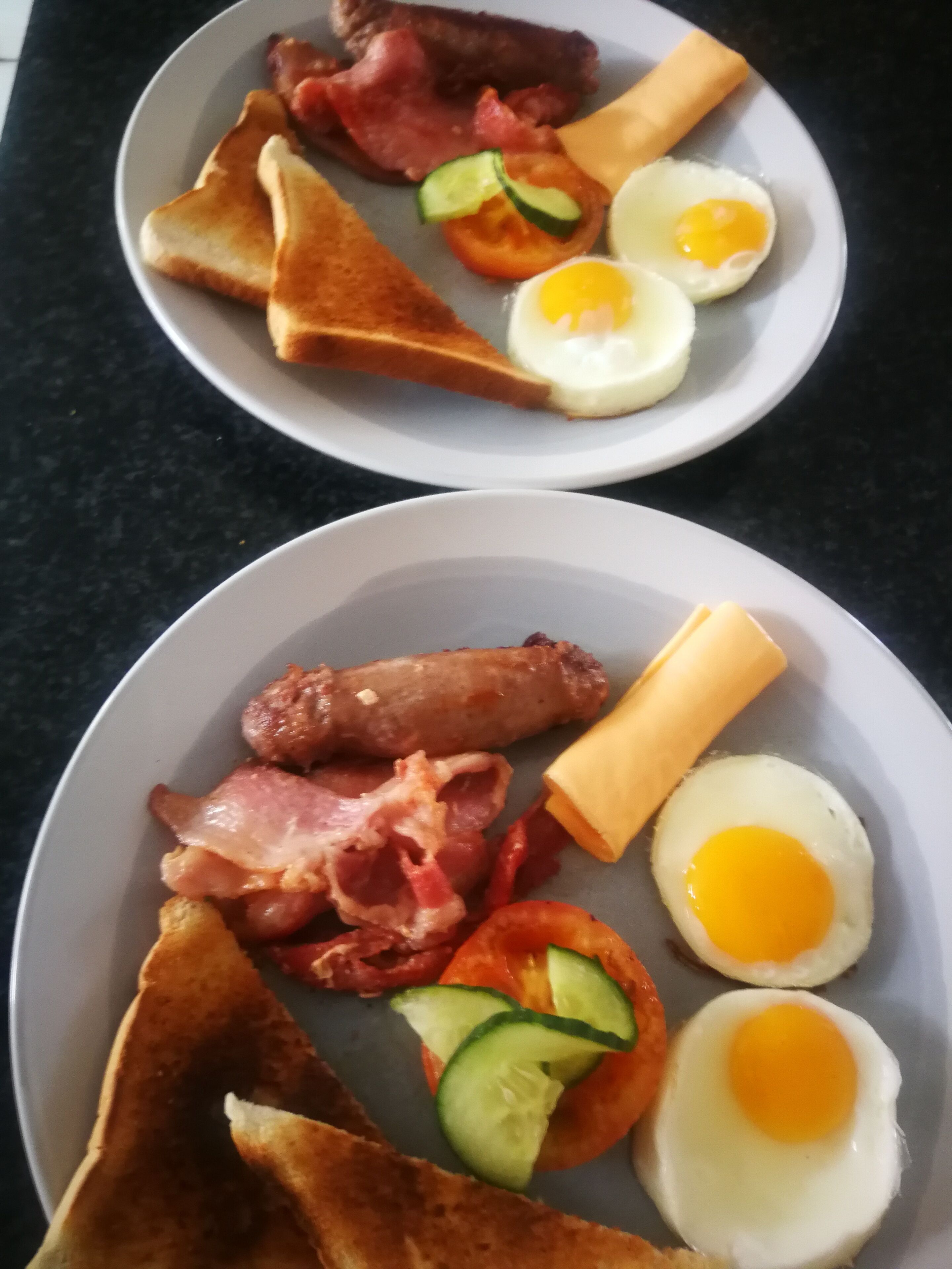 Dos platos de comida para el desayuno, con huevos, tocino, tostadas y tomates.