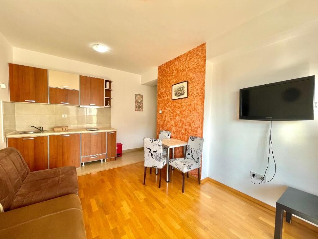 Een compacte woonruimte met kitchenette, eethoek en een wandgemonteerde flatscreen televisie.
