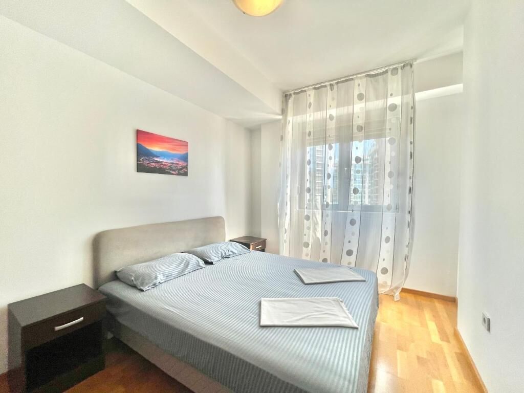 Ein Schlafzimmer mit einem Bett, einem Nachttisch, einem Gemälde und einem Fenster mit Vorhängen.