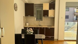 A compact kitchen with dark cabinets, a sink, and a dining area with a table and chairs. - Comfort Apartments Aleksic (Budva)