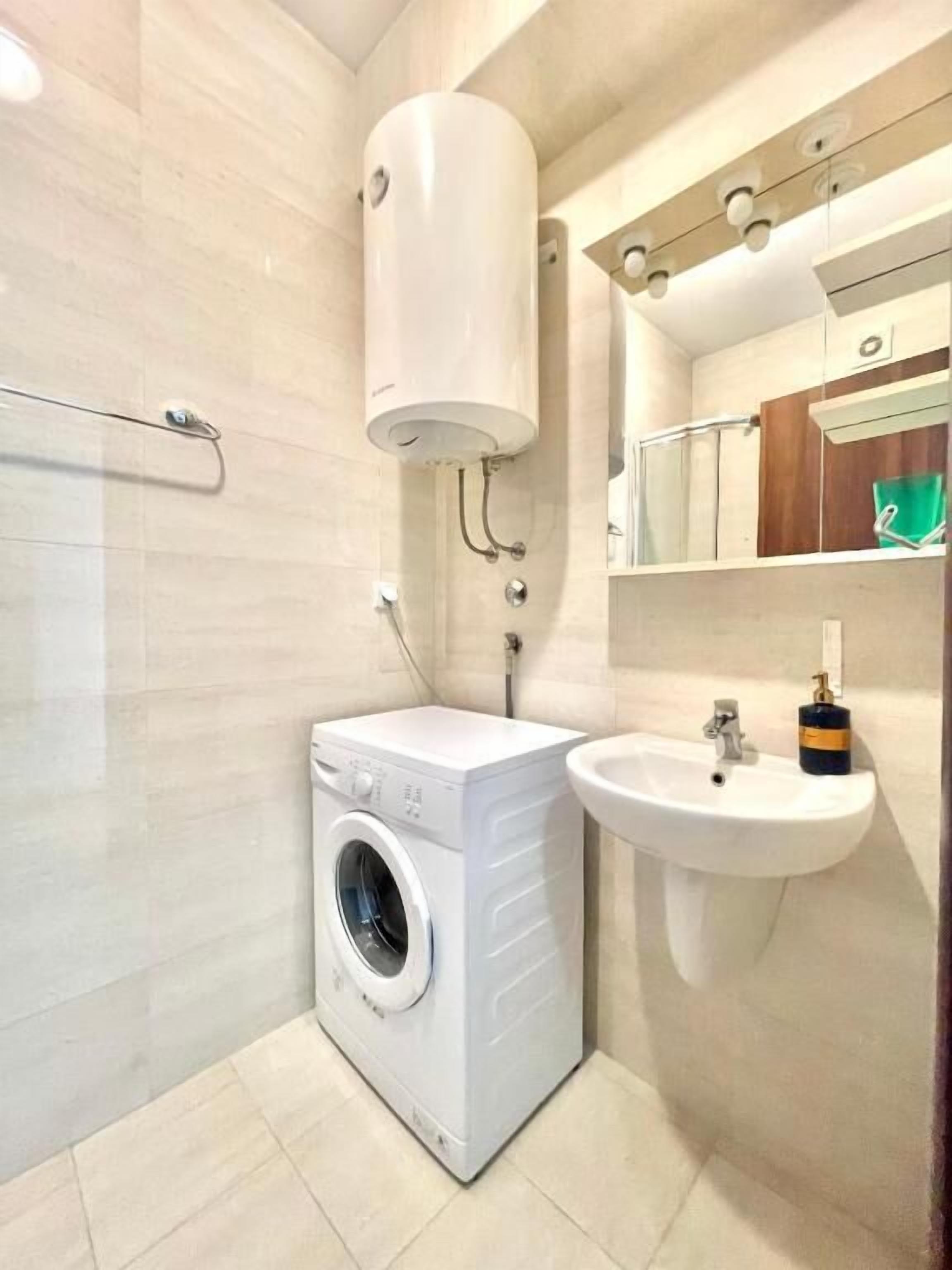 A compact bathroom with a built-in washing machine, a sink, and a mirror.
