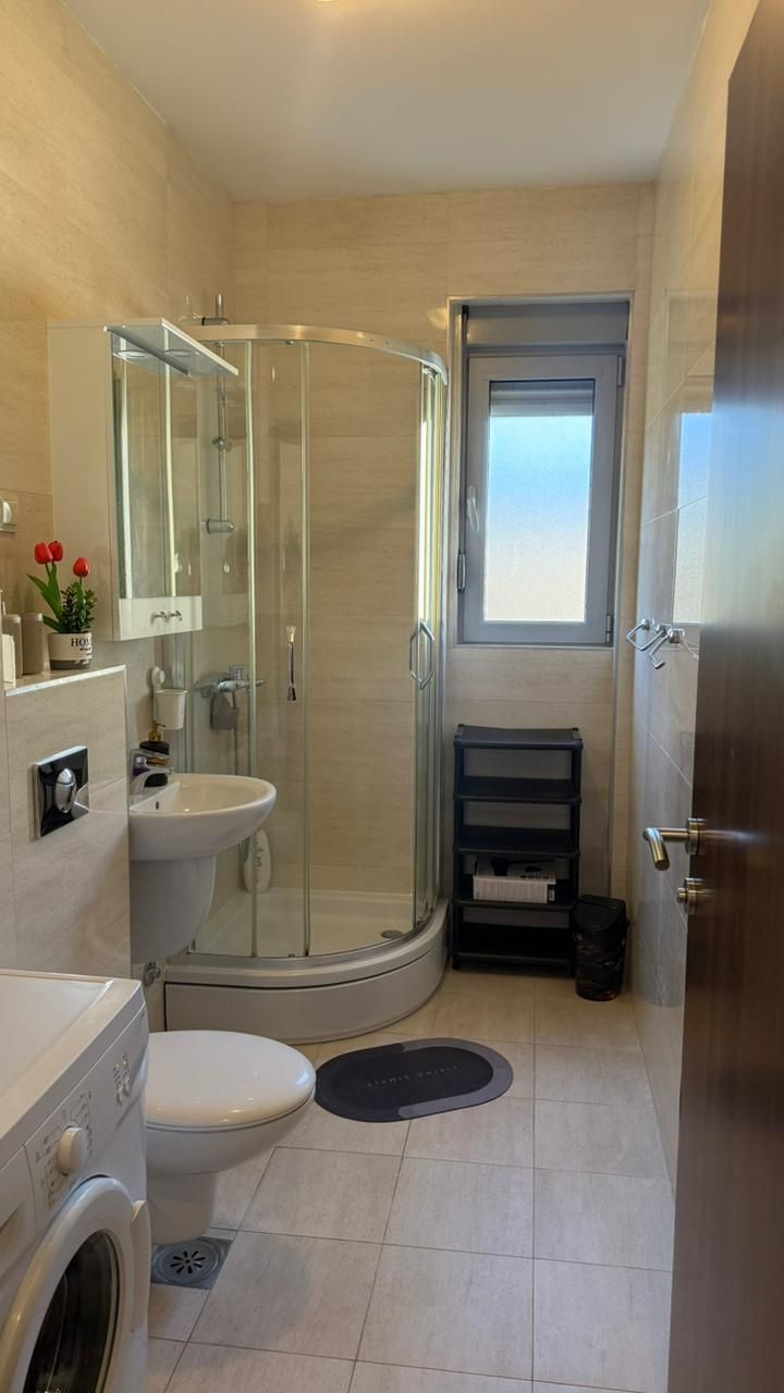 A compact bathroom with a glass shower enclosure, a sink, a toilet, and a washing machine.