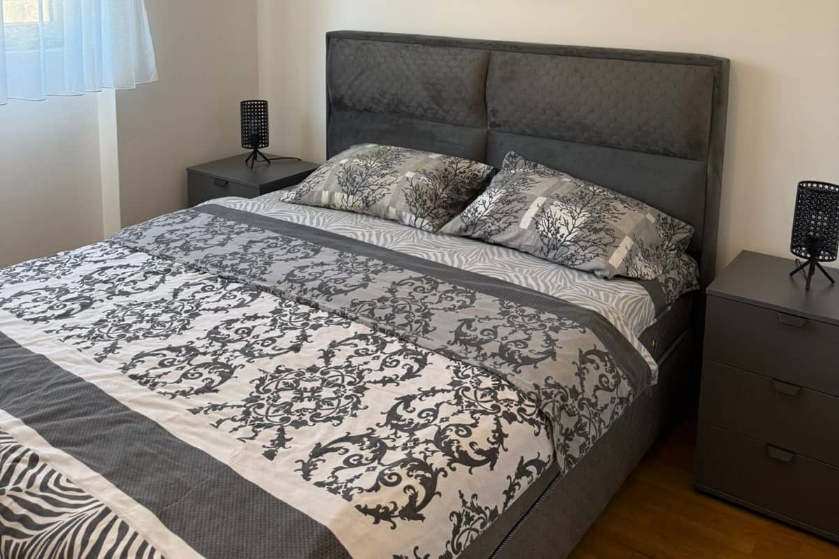 A bedroom with a bed, a nightstand, a dresser, a painting, and a window with curtains.