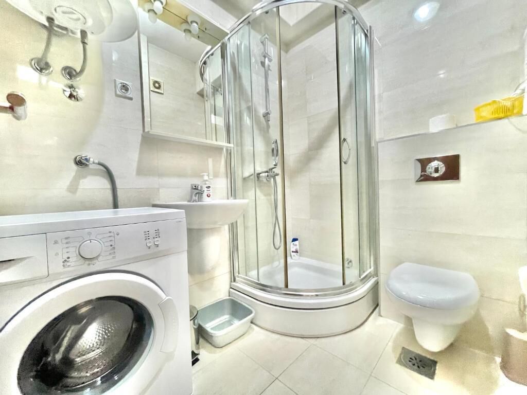 A modern bathroom with a glass-enclosed shower, a washing machine, and a toilet.