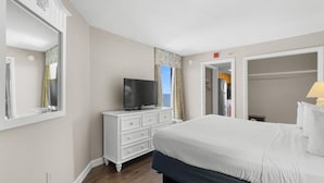 A hotel room with a large bed, a TV on a white dresser, and a wardrobe.
