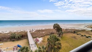 Blick auf einen Strand vom Balkon aus, mit Holzboden, Palmen und einem Sandstrand.
