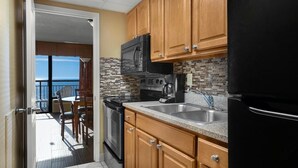 A kitchen with wooden cabinets, a black refrigerator, and a view to the outside.