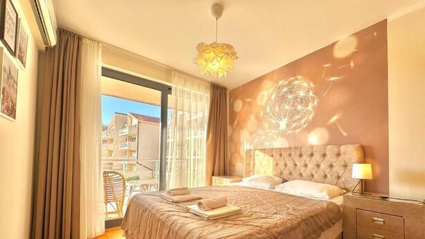 Habitación de hotel con una cama grande, una mesita de noche, una lámpara y vistas al exterior.