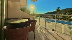 Un balcón con mesa y sillas, con vista a una piscina y un paisaje montañoso.
