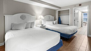 A hotel room with two beds, a nightstand, a lamp, and a view of the balcony. - 10th Flr Oceanfront Suite Includes Hot Breakfast (Myrtle Beach)