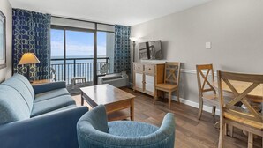 A modern living room with a sofa, chairs, a table, and a balcony with a view. - 10th Flr Oceanfront Suite Includes Hot Breakfast (Myrtle Beach)