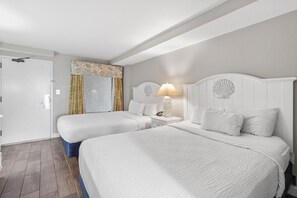 Two single beds with white bedding and matching headboard, a nightstand with a lamp, and a door.