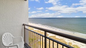 A balcony with a white chair, overlooking a beach with a sandy shore and calm waters. - Oceanfront Suite: 2 Queens Free Breakfast 11th Flr (Myrtle Beach)