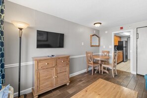 A dining area with a wooden table and chairs, a cabinet with drawers, a floor lamp, and a television mounted on the wall. - Oceanfront Suite: 2 Queens Free Breakfast 11th Flr (Myrtle Beach)