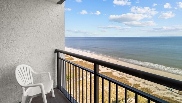 En balkon med en hvid plaststol, udsigt over stranden og havet.