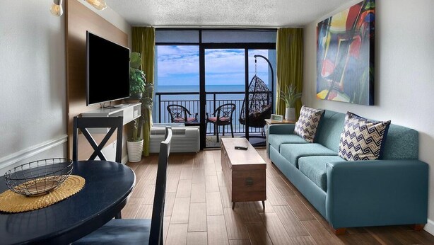 A modern living room with a sofa, TV, and dining area. - Magnificent Oceanfront Suite: 11th Flr (Myrtle Beach)