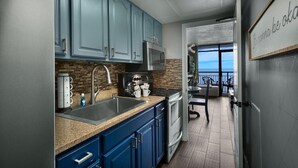 A modern kitchen with blue cabinets, stainless steel appliances, and a view to the outside. - Magnificent Oceanfront Suite: 11th Flr (Myrtle Beach)