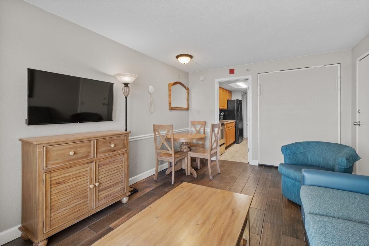 Een woonkamer met een houten kast, een televisie, een eettafel met stoelen en een blauwe bank.