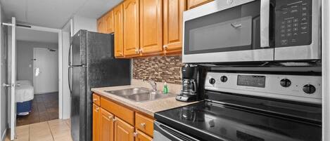 A kitchen with wooden cabinets, a stainless steel refrigerator, a microwave, a coffee maker, and a stove.