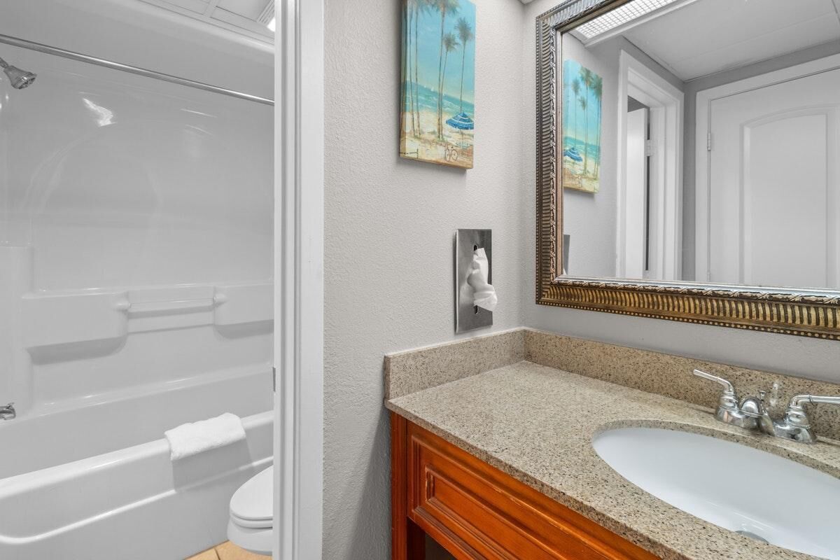 A bathroom with a shower, toilet, sink, and a large mirror.