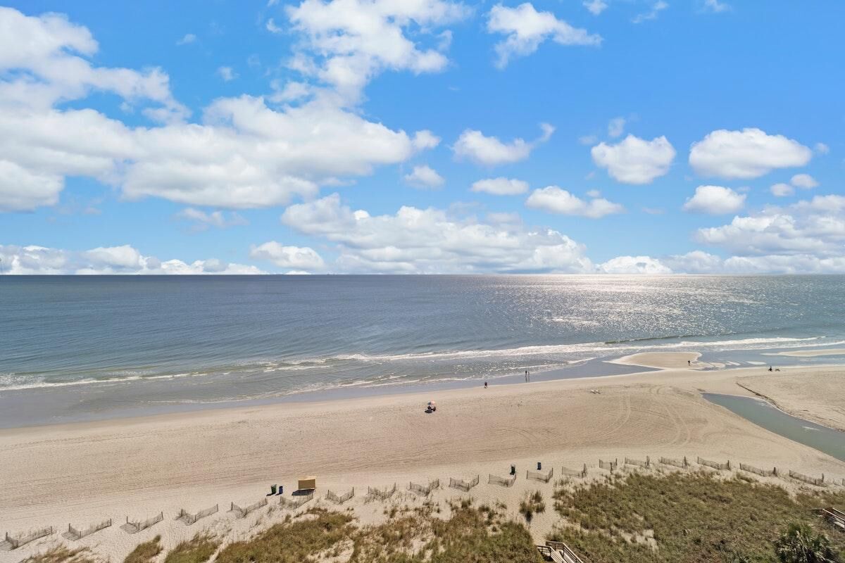 A beach with a sandy shore, a wooden fence, and a clear sky.