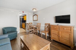 Ein Wohnzimmer mit Holztisch, blauem Sofa, Holzstühlen, einem Fernseher und einer Holzkommode.