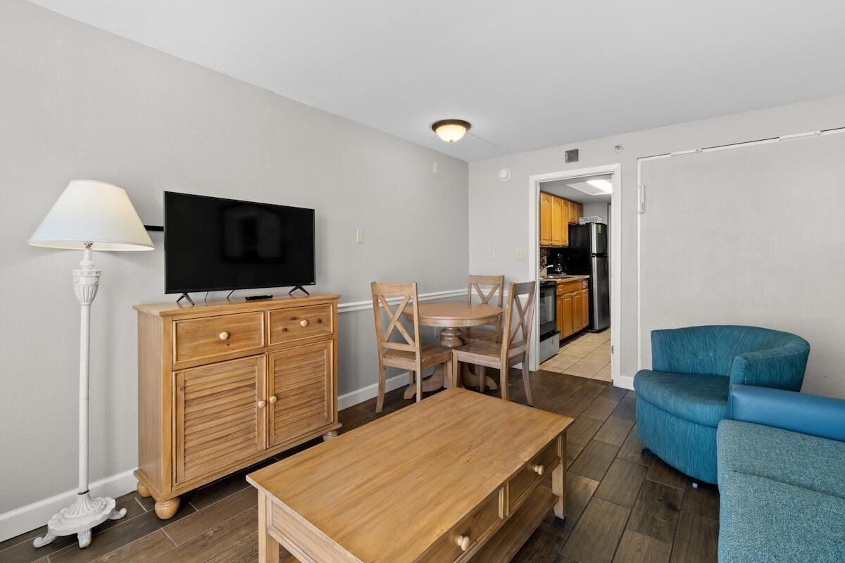A living room with a wooden table, a TV, a lamp, and a blue armchair.