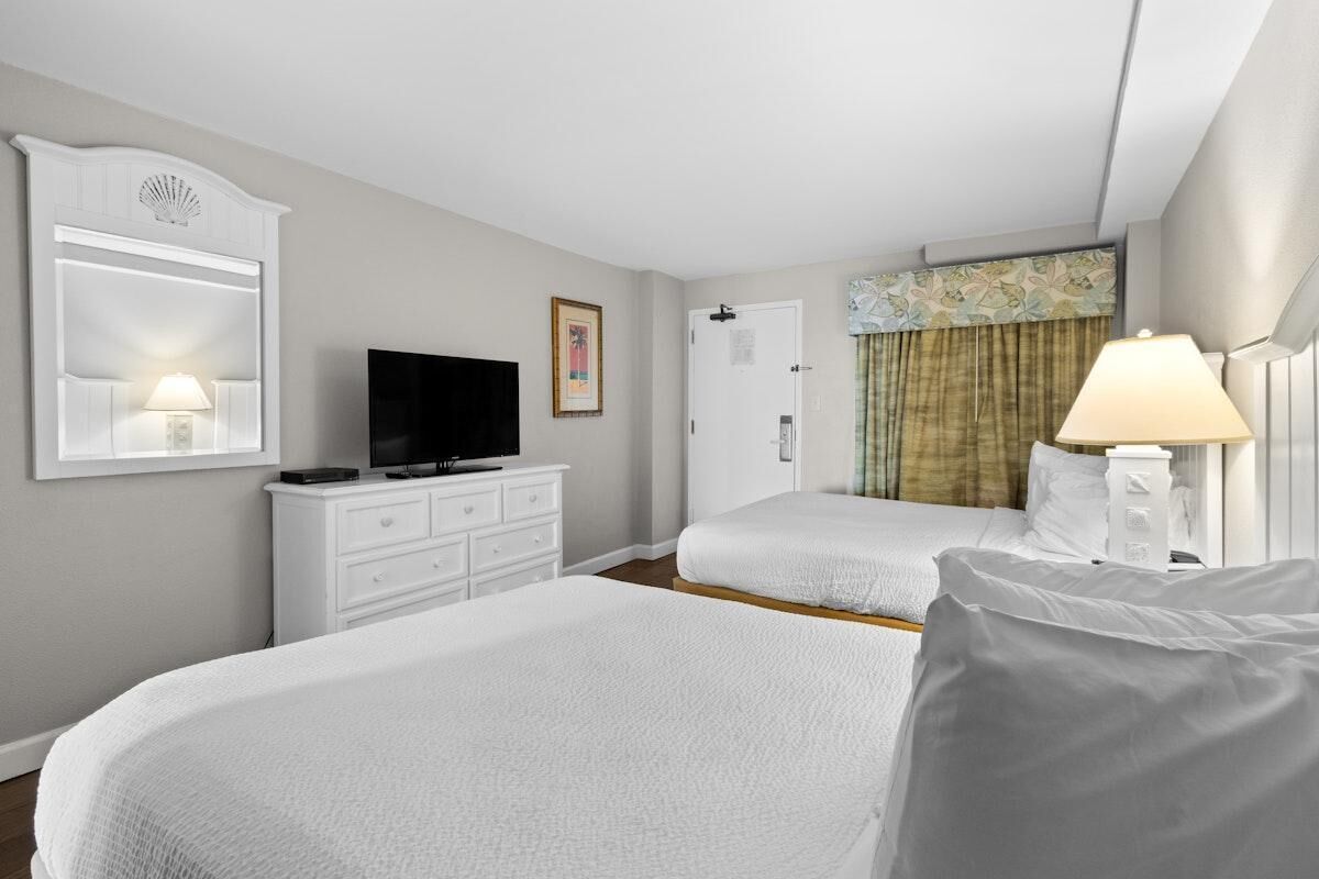 A hotel room with two beds, a television, a dresser, and a lamp.