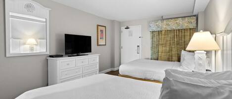 A hotel room with two beds, a television, a dresser, and a lamp.