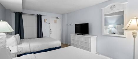 A hotel room with two beds, a television, a dresser, and a lamp.