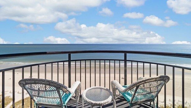 A balcony with wicker chairs and a small table, overlooking a beach with a clear sky. - Magnificent Oceanfront Ste 14th Flr w/Breakfast (Myrtle Beach)