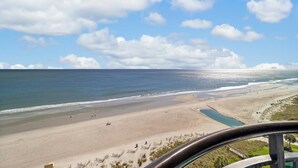 A beach with a clear sky, a sandy shore, and a few people walking. - Magnificent Oceanfront Ste 14th Flr w/Breakfast (Myrtle Beach)