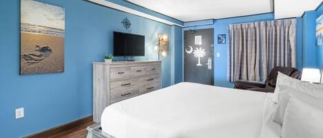 A bedroom with a large bed, a TV, a dresser, and a painting of a beach scene.