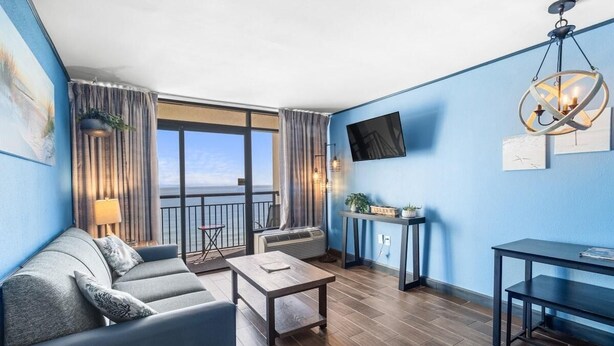 A modern living room with a sofa, coffee table, and a TV mounted on the wall. - Oceanfront King Suite: Free Breakfast 15th Floor (Myrtle Beach)