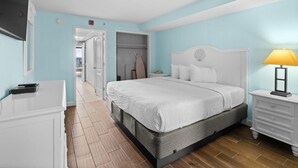 A bedroom with a bed, bedside table, lamp, wardrobe, and a door leading to another room.