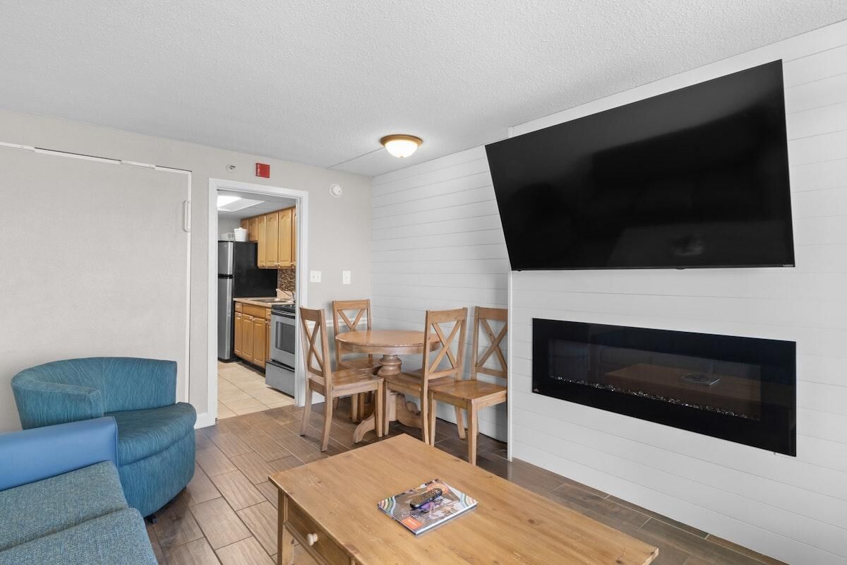 Een woonkamer met een televisie, open haard en een eethoek met houten stoelen en een tafel.
