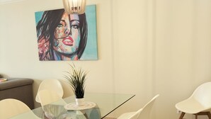 Un coin repas avec une table en verre, des chaises blanches, un luminaire suspendu et un tableau au mur.
