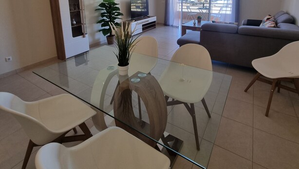 Un salon moderne avec une table à manger en verre, des chaises blanches, un canapé et un téléviseur.