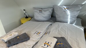Een netjes opgemaakt bed met gestreept beddengoed en kussens, elk voorzien van een logo.