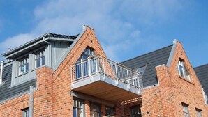 Een modern gebouw met een bakstenen gevel, grote ramen en een balkon met metalen hekwerk.