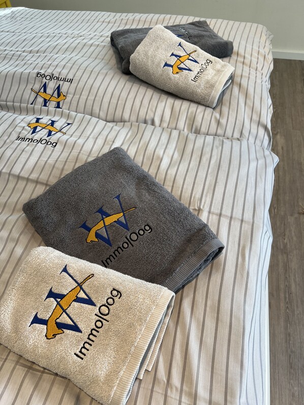 A bed with striped bedding and three folded towels with a logo and text.