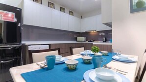 A modern kitchen with white cabinets, a black refrigerator, and a dining area with a blue tablecloth. - A Comfy & Cozy Suasana Suites in Johor Bahru (Johor Bahru)