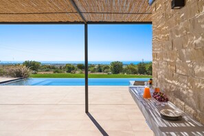 A poolside area with a view of the sea, a table with plates and drinks, and a stone wall. - Panoramic luxury villa with private pool in Sampieri - Di Casa In Sicilia (Sampieri)
