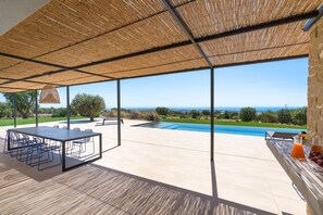 A spacious patio with a pool, outdoor seating, and a view of the ocean. - Panoramic luxury villa with private pool in Sampieri - Di Casa In Sicilia (Sampieri)