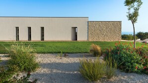 A modern building with a flat facade, large windows, and a stone wall section. - Panoramic luxury villa with private pool in Sampieri - Di Casa In Sicilia (Sampieri)