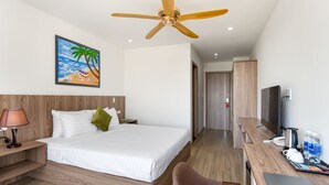 A hotel room with a bed, a desk with a laptop, a television, and a painting of a beach scene. - Vivi An Bang Hotel (Da Nang)