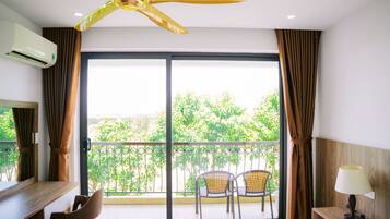 Habitación de hotel con ventilador de techo, balcón con sillas y vistas a zonas verdes.