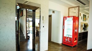 A hallway with a vending machine, a wooden floor, and a door leading to another room. - Vivi An Bang Hotel (Da Nang)