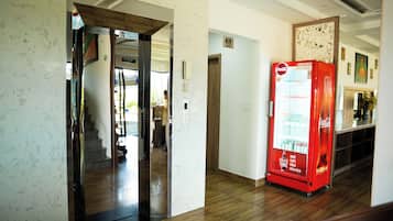 A hallway with a vending machine, a wooden floor, and a door leading to another room.