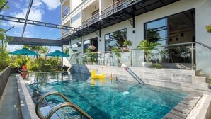 A swimming pool with a glass barrier, a yellow inflatable float, and a covered seating area with umbrellas. - Vivi An Bang Hotel (Da Nang)
